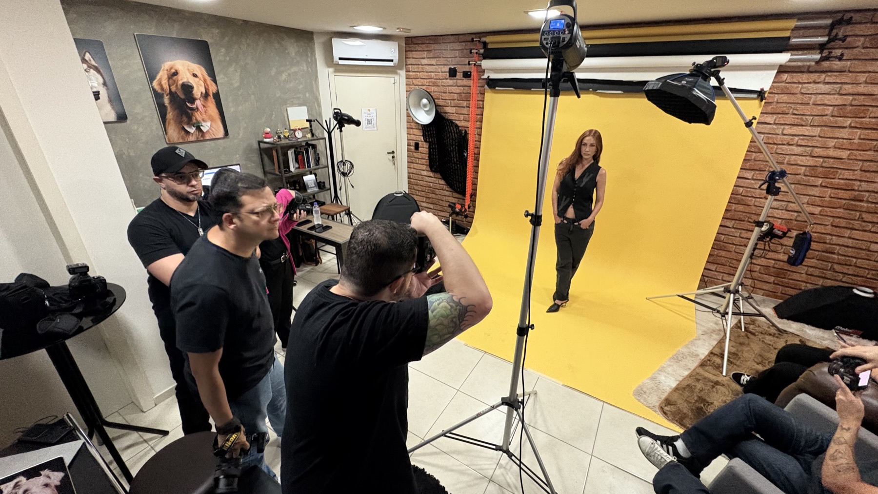 Participante do workshop fotografando a modelo em fundo amarelo enquanto a turma acompanha, no estúdio Jésus Lopes