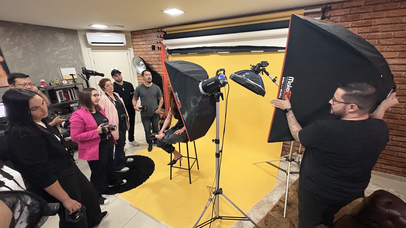Jésus Lopes posicionando um softbox enquanto a turma acompanha de câmera na mão